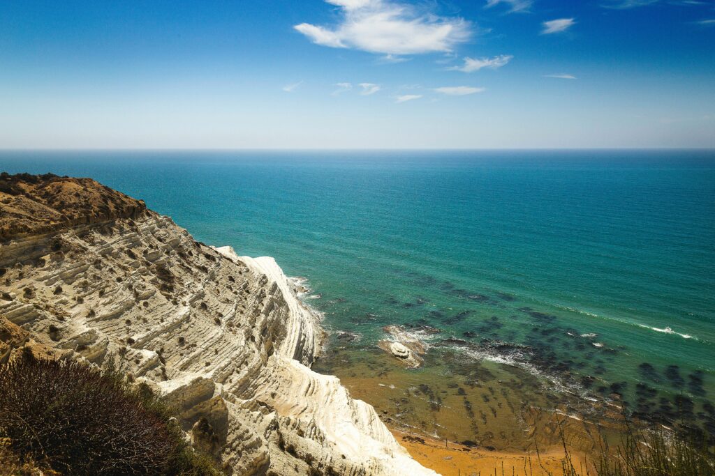 Stunning aerial view of a rocky coastal cliff with clear blue ocean under a bright sky.