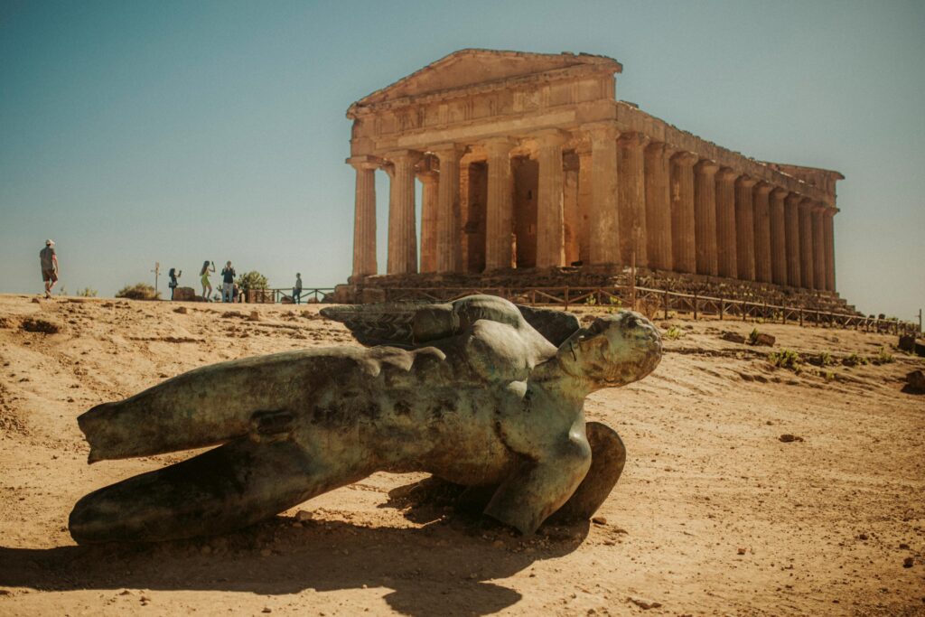 Photo of the Valley of the Temples in Agrigento, Italy featuring a fallen statue against a historical temple.