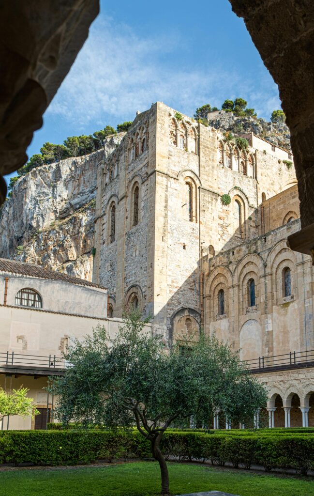 Monreale Cathedral with its stunning architecture under a clear sky, viewed from a courtyard.